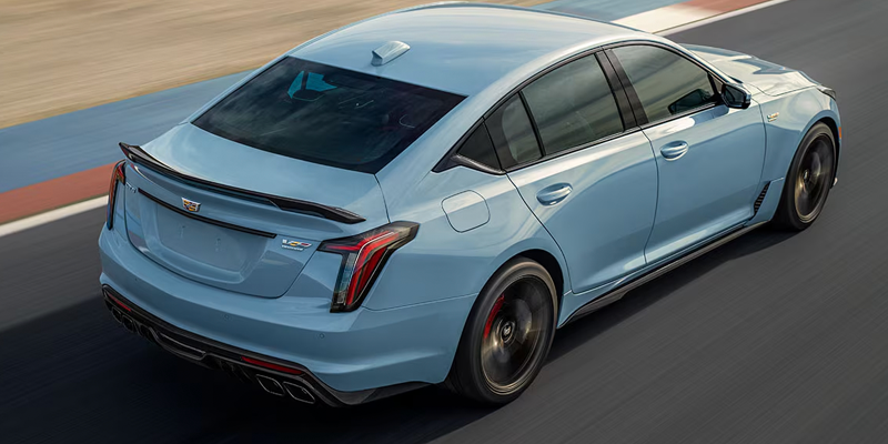 High-angle rear view of a light blue Cadillac CT5-V Blackwing sedan driving along a racetrack.