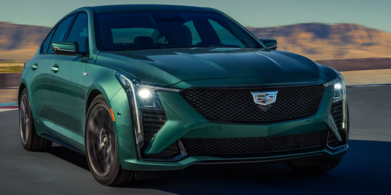 A green Cadillac CT4 sedan driving along a open track with desert hills in the background.