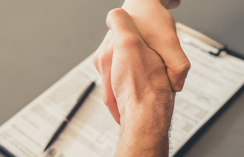 A close-up of two people shaking hands over a clipboard with a contract and a pen.